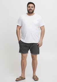 Fehér, rövid ujjú póló, mellzsebes kialakítással, sötét szürke, felhajtott szárú shortsokkal és barna szandálokkal párosítva. Egyszerű dizájn, laza illeszkedés.