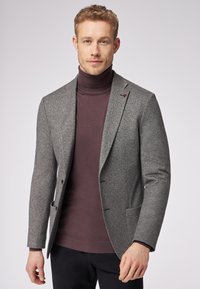 Gray herringbone blazer with a slim fit, notched lapels, and two front pockets, layered over a dark purple turtleneck.