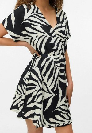 Woman wearing short black and white zebra-print dress with V-neck and short sleeves, hand resting on hip.
