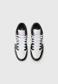 Melnas un baltas kedas ar perforētu purngali, rozā akcentiem un plakaniem baltajiem šņorēm. Uz mēles ir Air Jordan logo.