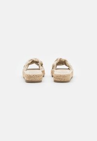 Sandales espadrilles beiges avec un empeigne tressée, semelles en corde de jute, talon plat et texture lisse. Le design présente un dos ouvert.