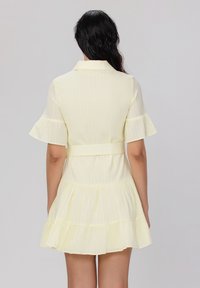 Robe jaune à rayures avec des manches courtes évasées, une taille ceinturée et une jupe à volants. Texture de tissu lisse, design décontracté.