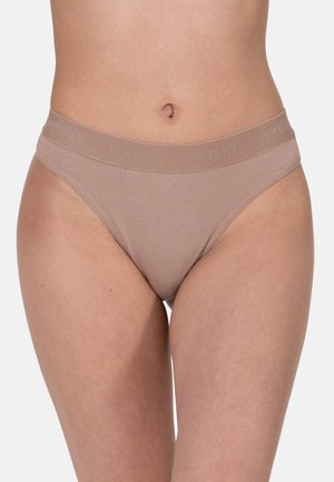 Donna che indossa biancheria intima beige senza cuciture a taglio alto con fascia elastica con marchio, ritagliata a metà corpo su sfondo uniforme.