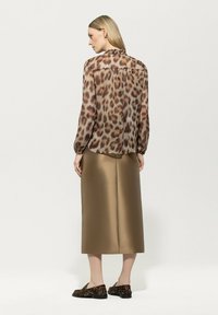 Lässige, durchsichtige Bluse in Braun mit einem Leopardenmuster, kombiniert mit einem matten, bronzefarbenen Rock. Schwarze Slipper mit passendem Leopardenmuster.