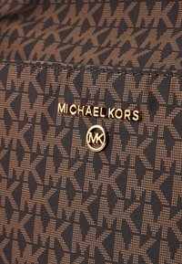 Țesătură maro cu un model de logo-uri interconectate "MK", cu un logo aurit "MICHAEL KORS" și un accent circular aurit "MK".
