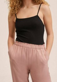 Czarna prążkowana koszulka na cienkich ramiączkach w połączeniu z jasnoróżowymi, spodniami o elastycznym pasie, które mają boczne kieszenie i gładką teksturę materiału.