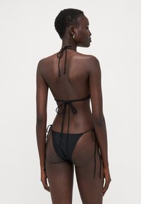 Čierny bikini s halter výstrihom a viazačkami. Minimalistický dizajn s nízkym pásom a tenkými bočnými viazačkami. Hladká textúra.