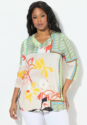 Blouse ample avec un col en V, ornée d'un motif floral rouge, jaune et vert sur un fond beige doux. Manches trois-quarts.