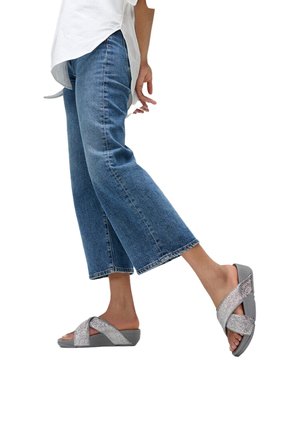 Grijze plateauzandalen met gekruiste, gestructureerde zilveren bandjes. Draagt bij een cropped spijkerbroek met een ontspannen pasvorm en rafelige zomen.