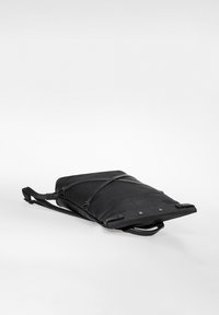 Schwarzer schlanker Laptop-Rucksack mit verstellbarem Schultergurt und vorderer Reißverschlusstasche, flach auf einer weißen Oberfläche liegend.