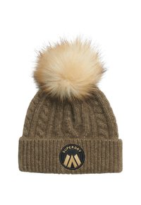 Bruine cable-knit muts met namaakbont pompon bovenop, voorzien van een ronde zwart-gouden "SUPERDRY" logo patch op de omgeslagen band.