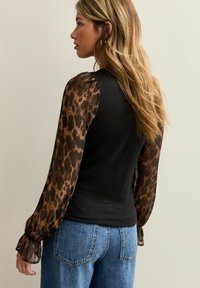 Zwart strak topje met doorschijnende luipaardprintmouwen en elastische manchetten, gecombineerd met hooggetailleerde blauwe denim. Licht textuur, casual stijl.