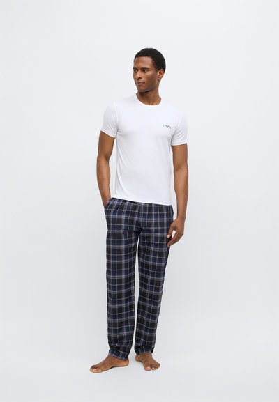 Bílé bavlněné tričko s malým logem na hrudi, doplněné modrými a černo-modrými károvanými pyžamovými kalhotami, které mají volný střih a měkkou texturu.