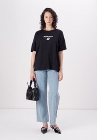 Black oversized t-shirt with white logo, paired with light blue denim jeans featuring white speckles. Accessorized with a black handbag and heels.