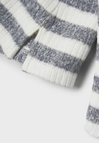Teksturoitu neulepusero, jossa on vaihtelevat paksut ja ohut harmaan ja valkoisen raidat. Ribbaat huput ja helmat tuovat rakennetta.