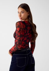 Długorękawowa bluzka z siateczki o czarnym tle z czerwonym kwiecistym wzorem, w dopasowanym fasonie z okrągłym dekoltem i przezroczystą strukturą.