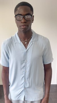 Lys blå kortærmet skjortebluse lavet af et glat stof, med en subtil glans og en afslappet pasform. Sammen med en hjerteformet halssmykke.