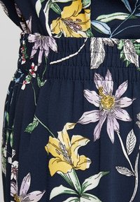 Tissu bleu marine avec une taille élastique présentant un motif floral de fleurs jaunes, lavandes et blanches avec des feuilles vertes.