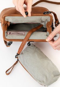 Borsa in pelle marrone con un interno in tessuto a righe. Presenta una pochette staccabile e hardware nero. La parte superiore si apre con una zipper.