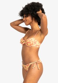 Bikini-set in een roze en gele bloemenprint. Bh-top met beugel en strikdetail, verstelbare bandjes; onderkant met touwtjes aan de zijkanten en minimale bedekking.