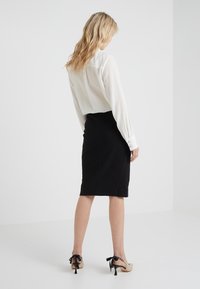 Lättviktig vit blus med krage, tillsammans med en figurnära svart blyertskjol. Framhävt beiget klackskor med svarta bandaccent.