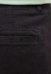 Czarne bawełniane spodnie o gładkiej fakturze, z łatką kieszeni oznaczoną etykietą "MUSTANG" oraz szyciem dopasowanym wzdłuż krawędzi.