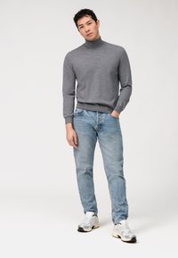 Grauer Rollkragenpullover mit gerippten Bündchen, kombiniert mit hellblauen Jeans. Getragen mit weißen und silbernen Sneakers, minimalistischem Stil.