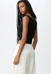 Zwart cropped tanktop met ronde hals en zilveren knopen, gecombineerd met hoge taille witte broeken met achterzakken en plooien.