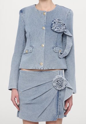 Conjunto de chaqueta y falda de mezclilla azul claro con botones dorados y detalles de rosetas de tela a juego en el pecho y la cadera.