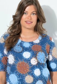 Top azul de manga corta con un patrón de explosiones de varios tamaños en colores naranja, blanco y azul claro sobre un fondo sólido.