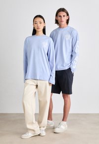 Light blue long-sleeve shirts with white decorative patterns, paired with cream-colored pants and dark shorts, white sneakers.
