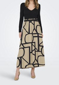 Top negro de manga larga combinado con una falda beige de longitud completa que presenta un atrevido patrón geométrico negro. Tejido suave; tacones beige con tiras al tobillo.