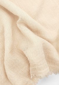 Tessuto di lino beige chiaro con una trama morbida e testurizzata, che si drappeggia in morbide pieghe. I bordi hanno una finitura sfilacciata.