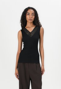 Canotta nera a coste con un bordo in pizzo decorativo lungo il collo a V. Presenta una silhouette aderente e design senza maniche, abbinata a pantaloni marroni.