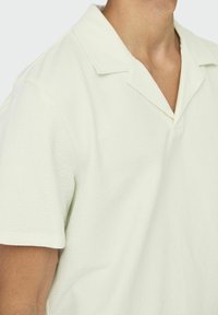 Kortärmad, ljusgrön polo skjorta med en strukturerad våffelväv. Har en krage och en avslappnad passform, med en djup V-ringning.