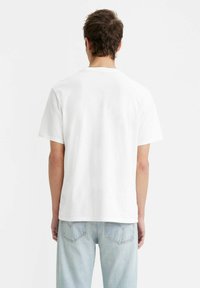 Biała bawełniana koszulka z krótkim rękawem i luźnym krojem, z prostym, nieozdobionym wzorem. Noszona z jasnoniebieskimi dżinsami.