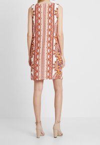 Ärmelloses Kleid mit einem bunten floralen und geometrischen Muster in Orange und Rot auf weißem Hintergrund, mit einem knielangen Saum.