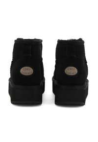 Un paio di stivali neri alla caviglia con suole piatte, foderati in morbido tessuto e con il logo "EMU Australia" sul retro di ciascun tallone.