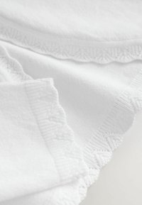 Tela de algodón blanca con un acabado texturizado, que presenta un borde de encaje decorativo a lo largo de los bordes y una apariencia suave y esponjosa.