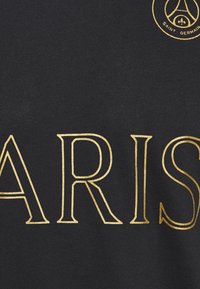 Černé tričko z látky s velkými zlatými nápisy "PARIS" a na vrchu kulatým logem s textem "SAINT-GERMAIN."