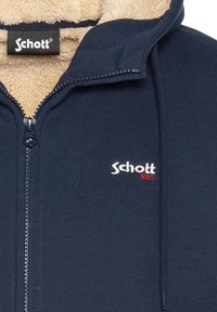 Marineblauw jack met ritssluiting en een met fleece gevoerde capuchon, met een wit en rood geborduurd logo op de borst en een gestructureerde buitenzijde.