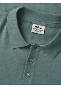 Camisa polo verde claro con cuello, dos botones y tela texturizada. Presenta una etiqueta que dice "R.D.D. ROYAL DENIM DIVISION."