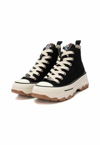 Sneaker alte nere in canvas con lacci crema, punta bianca, suola chunky bianca e beige, e dettaglio del logo sulla linguetta.