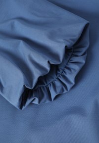 Tissu bleu avec une texture douce et lisse, présentant un détail de volant froncé sur un bord, mettant en valeur un design fluide.