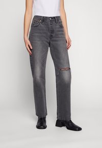 Grå denimjeans med en avslappnad passform, med knäskador, fem fickor och bälteshällor, i kombination med svarta ankelboots.