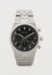 Ασημένιο ρολόι χειρός χρονογράφου από ανοξείδωτο ατσάλι με μαύρο καντράν, τρεις υποκαντράν, παράθυρο ημερομηνίας στη θέση 4 η ώρα και ασημένιο μπρασελέ με συνδέσμους.