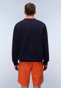 Marineblå hettegenser med rund hals og lange ermer, sammen med oransje shorts. Glatt tekstur og minimalistisk design.