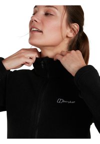 Veste en polaire noire avec col haut, fermeture éclair et logo brodé. Texture douce avec des manches longues et une coupe décontractée.