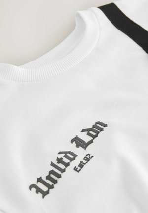 T-shirt en coton blanc avec un col rond côtelé, des accents noirs aux épaules et un texte brodé en gris foncé. Texture lisse.