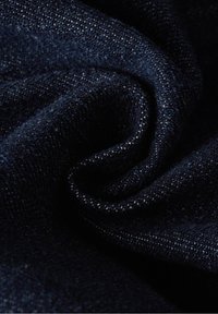 Tumma farkkukangas, jossa on teksturoitu pinta, syvän laivastonsinisessä värissä ja hienovaraisessa kiillossa, taiteltu kerroksiin näyttämään pehmeää kudontakuviota.